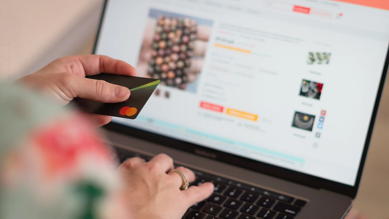 Person holding a credit card while shopping online on a laptop.