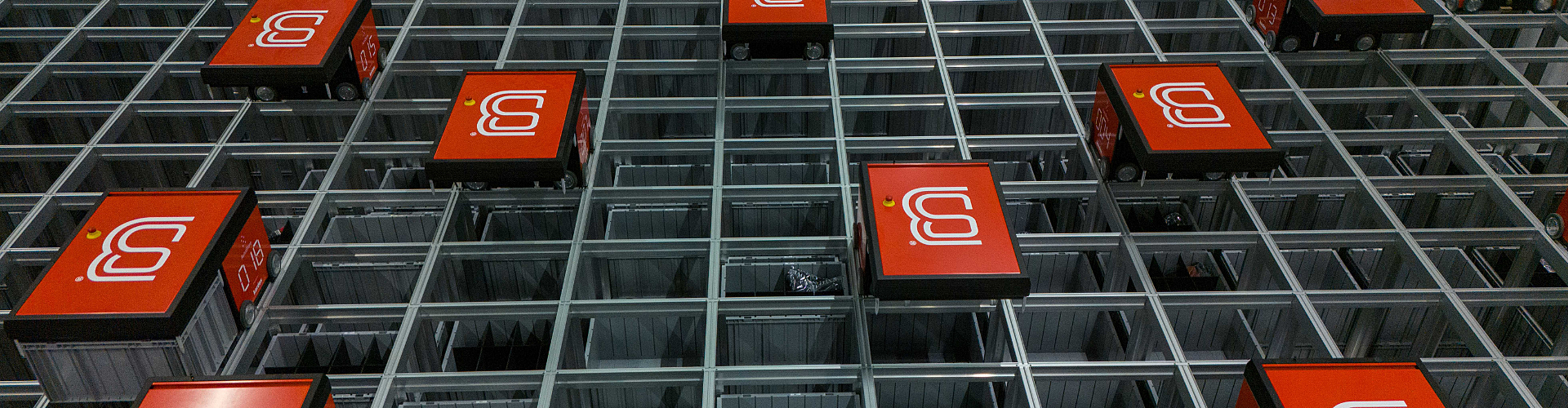 A grid of automated red robotic units on tracks, used for sorting or storage in a warehouse setting.