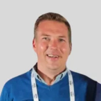 Man wearing a blue sweater and a lanyard, smiling at the camera against a plain background.